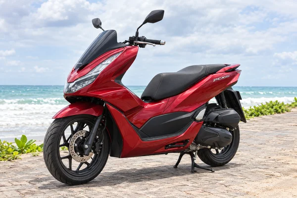 Red Honda PCX160, front-left view, beside the ocean