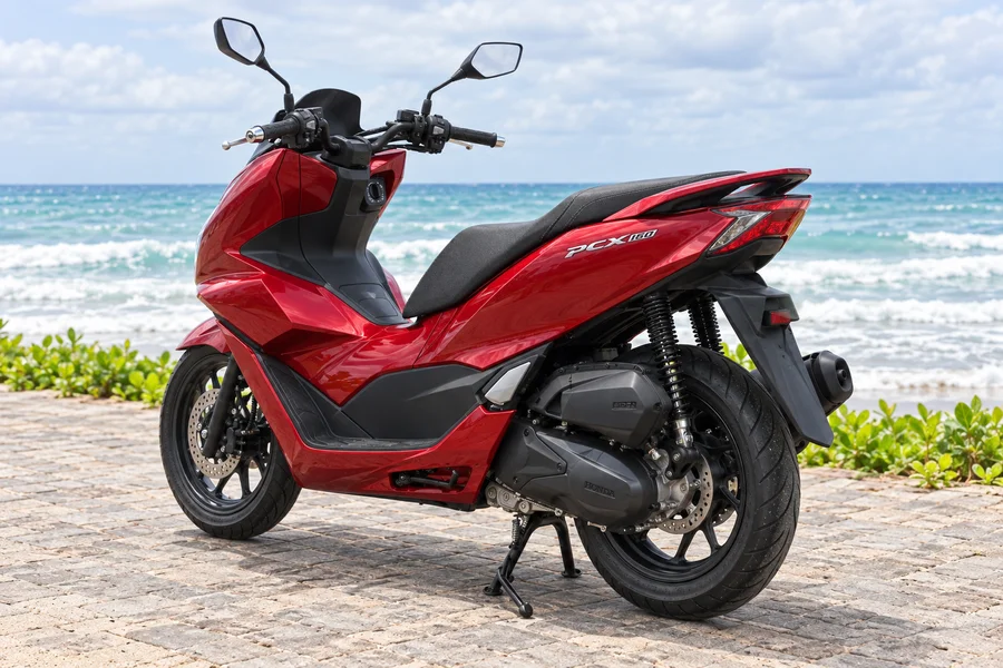 Red Honda PCX160, front-left view, beside the ocean