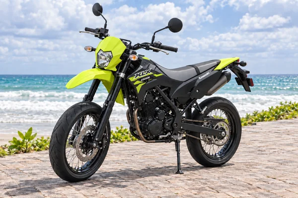 Neon-green and black Kawasaki KLX230 Supermoto, front-left view, beside the ocean